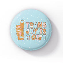 Load image into Gallery viewer, Single light blue badge on a white background with gingerbread present illustrations and the text &quot;Trans Joy is a Gift.