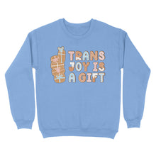 Load image into Gallery viewer, Cornflower blue sweatshirt featuring the phrase &#39;Trans Joy Is A Gift&#39; styled like gingerbread cookies, with a stack of gifts to the left in pastel pink, blue, and white hues.