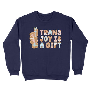 Oxford navy sweatshirt adorned with the phrase 'Trans Joy Is A Gift' in a gingerbread-inspired design, flanked by a vertical stack of pastel-coloured presents.