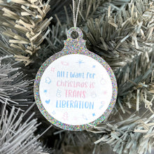Load image into Gallery viewer, Close up of a white Christmas tree displaying a silver glitter bauble featuring the text All I Want for Christmas is TRANS LIBERATION surrounded by Christmas icons such as candy canes and stockings, all in the colours of the transgender flag; pink, blue, and white.