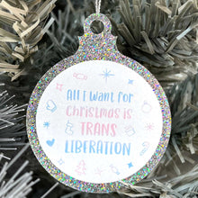 Load image into Gallery viewer, Close up of a white Christmas tree displaying a silver glitter bauble featuring the text All I Want for Christmas is TRANS LIBERATION surrounded by Christmas icons such as candy canes and stockings, all in the colours of the transgender flag; pink, blue, and white.