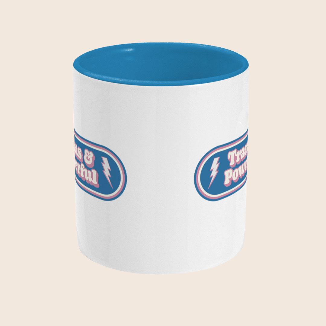 Front view of Trans & Powerful mug with blue handle and interior, featuring a retro badge-style design in trans pride colours on a white ceramic mug