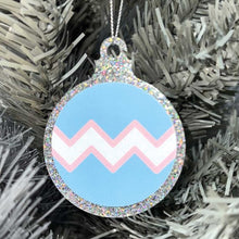 Load image into Gallery viewer, Close up of a white Christmas tree displaying a silver glitter bauble featuring a classic zig zag design in the colours of the transgender pride flag.