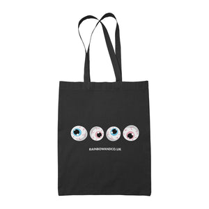 A black tote bag featuring four cartoonish eyeballs arranged in a row. Each eyeball has a different coloured iris, representing the transgender flag: one with a light blue iris, one with a pink iris, one with another light blue iris, and one with another light pink iris. Below the eyeballs, the text reads "RAINBOWANDCO.UK".