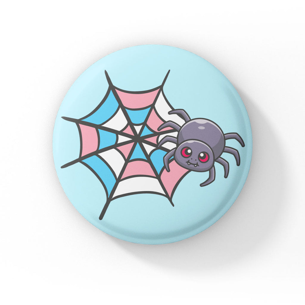 A circular badge showcasing a cute grey spider with pink eyes on a web coloured in blue, pink, and white, representing the transgender pride flag. The badge has a light blue background.