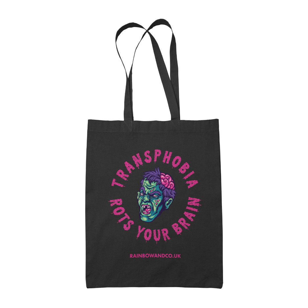 A black tote bag featuring a similar design to the "Homophobia Rots Your Brain" tote, but with the text "Transphobia Rots Your Brain" instead. The design includes a zombie face illustration and the website "RAINBOWANDCO.UK" at the bottom.