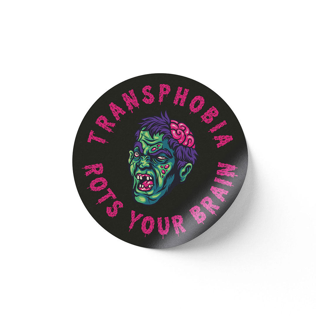 A round black sticker with a graphic of a green zombie face with an exposed brain. The words "Transphobia Rots Your Brain" are written in bold pink letters around the zombie illustration.