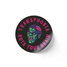 Load image into Gallery viewer, A round black sticker with a graphic of a green zombie face with an exposed brain. The words &quot;Transphobia Rots Your Brain&quot; are written in bold pink letters around the zombie illustration.