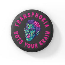 Load image into Gallery viewer, A round badge with a black background featuring a cartoon zombie head with green skin, purple hair, and exposed brain. The text &quot;TRANSPHOBIA ROTS YOUR BRAIN&quot; is written in bold, dripping pink letters around the zombie head.