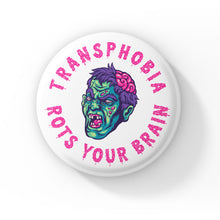 Load image into Gallery viewer, A round badge with a white background featuring a cartoon zombie head with green skin, purple hair, and exposed brain. The text &quot;TRANSPHOBIA ROTS YOUR BRAIN&quot; is written in bold, dripping pink letters around the zombie head.