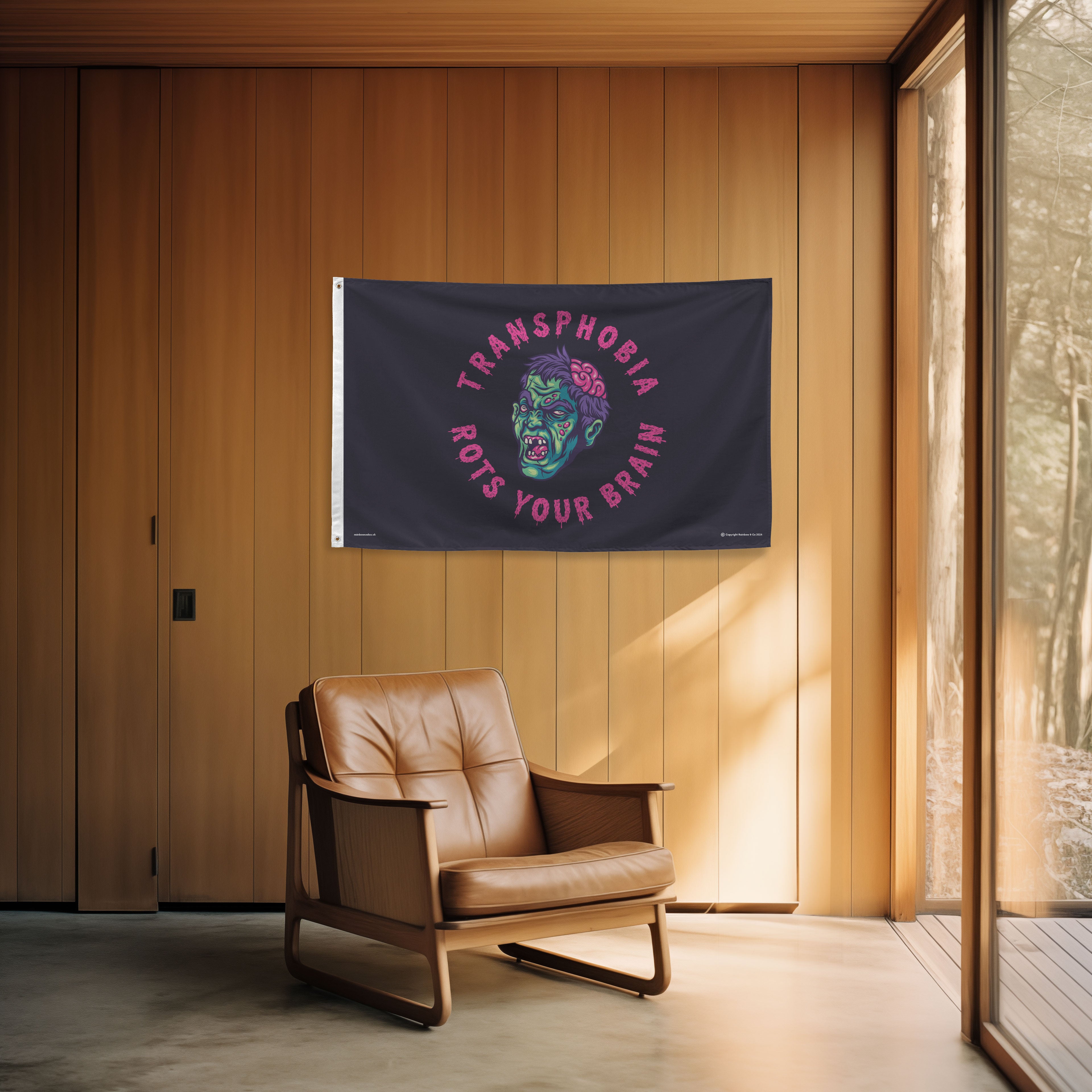 Flag with a Transphobia Rots Your Brain design and text hanging on a wooden wall above a brown leather chair.