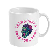 Load image into Gallery viewer, The right side of a white ceramic mug, showing a partial view of the zombie-like face design. The pink text &quot;TRANSPHOBIA ROTS YOUR BRAIN&quot; curves around the image, emphasizing the anti-transphobia message.