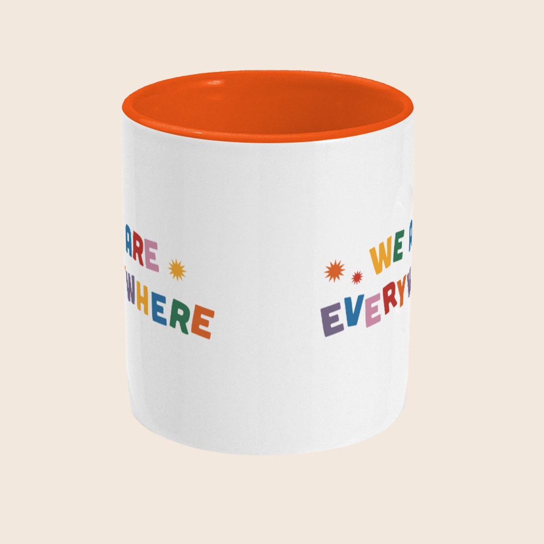 White ceramic mug with an orange handle and orange interior, featuring the phrase “We Are Everywhere” in colourful retro-style lettering on the front.