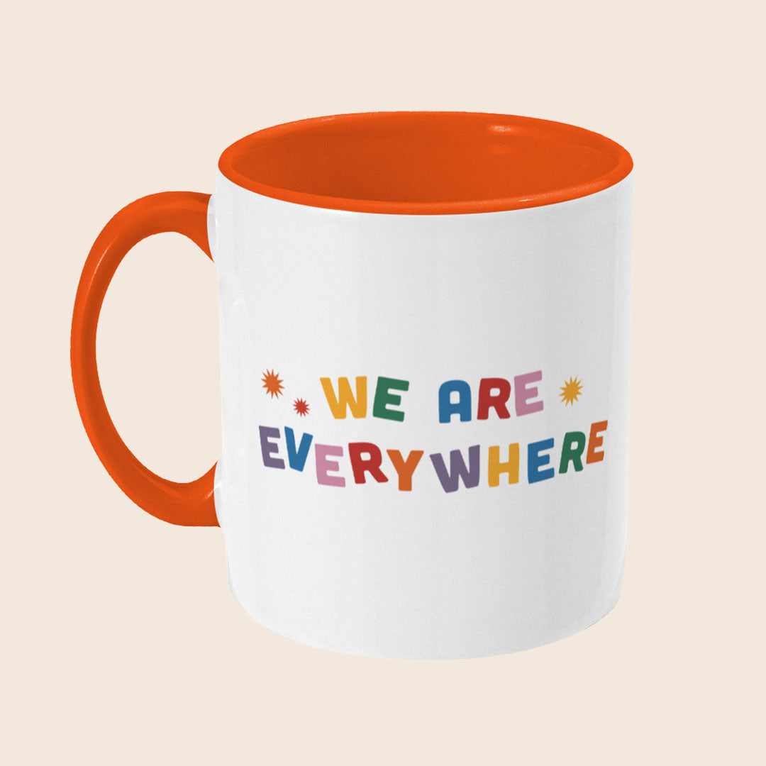Angled view of a white ceramic mug with an orange handle and interior, showing the “We Are Everywhere” design wrapping around the mug.
