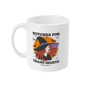 A white ceramic coffee mug with the handle on the left. The mug shows the slogan Witches for Trans Rights with an illustrated graphic of a witch with bats flying around her hat