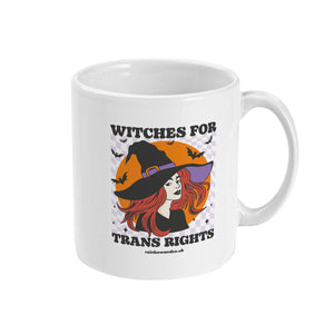 A white ceramic coffee mug with the handle on the right. The mug shows the slogan Witches for Trans Rights with an illustrated graphic of a witch with bats flying around her hat