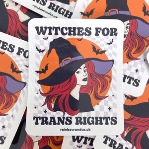A pile of glossy stickers with one stand out sticker in the foreground. The stickers feature the slogan 'Witches For Trans Rights' alongside an image of a witch surrounded by bats.