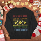 A black crewneck sweatshirt with a colorful Christmas-themed graphic reading 'DON WE NOW OUR GAY APPAREL' surrounded by holiday decorations like ornaments, gifts, pinecones, and a stocking on a wooden surface.