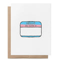 White greeting card featuring a "Hello, my name is" name badge in the colours of the trans pride flag with space to write a new name, with a brown kraft envelope behind.
