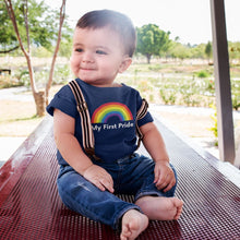 Load image into Gallery viewer, A young child with short dark hair wearing blue jeans with fabric braces and a navy blue My First Pride t shirt from Rainbow &amp; Co
