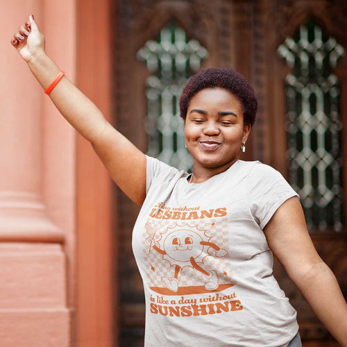 Black woman with a big smile on her face wearing a Rainbow & Co 'A Day Without Lesbians is Like a Day Without Sunshine' t shirt.