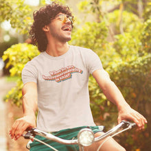 Load image into Gallery viewer, Retro style photo of a man wearing large vintage sunglasses and riding a bicycle. He is wearing a &#39;What in the heteronormativity is this?&#39; shirt from Rainbow &amp; Co