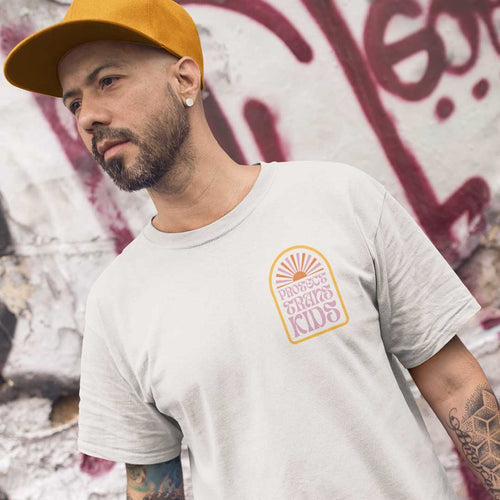 White man with a beard wearing a mustard coloured baseball cap and a Protect Trans Kids shirt from Rainbow & Co