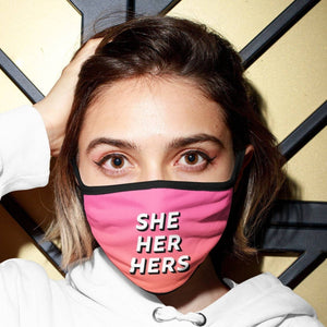 Person wearing a pink/orange gradient coloured face mask with SHE HER HERS pronouns on it.